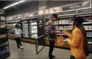  ?? ELAINE THOMPSON—ASSOCIATED PRESS ?? In this Jan. 22, 2018, file photo, a worker, right, looks at the ID of a shopper at the wine and beer area inside an Amazon Go store in Seattle. Get ready to say good riddance to the checkout line. A year after Amazon opened its first cashier-less store, startups and retailers are racing to get similar technology in other stores throughout the world, letting shoppers buy groceries without waiting in line.