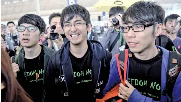  ?? — AFP photo ?? Hong Kong student leader Alex Chow (centre) smiles next to Nathan Law (left) and Eason Chung as they are surrounded by pro-democracy protesters at Hong Kong’s internatio­nal airport before an attempt to board a flight to Beijing.