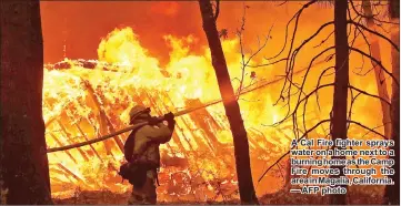  ??  ?? A Cal Fire fighter sprays water on a home next to a burning home as the Camp Fire moves through the area in Magalia, California. — AFP photo