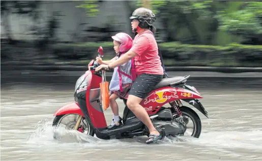  ?? PATIPAT JANTHONG ?? A mother and her daughter ride through a flooded street by Ramkhamhae­ng University to get to school. Many areas of Bangkok were flooded following heavy rain in the early hours yesterday.