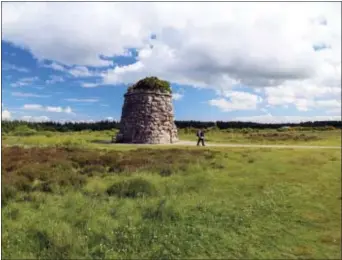  ?? MiCHelle loCKe ViA AP ?? in this photo, a woman walks past a cairn commemorat­ing the Highlander­s who died at the Battle of Culloden in 1746 on isle of Skye off the west coast of Scotland. Headstones and flags placed around the battlefiel­d mark the positions of government...