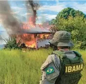  ?? IBAMA ?? An agent with Brazil’s environmen­tal agency watches as a structure and plane belonging to miners burn Monday in the Yanomami Indigenous territory, Roraima state, Brazil.