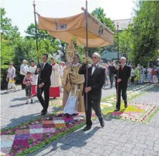  ?? FOTO: STILLER ?? Pfarrer Claus Blessing trägt die Monstranz mit dem verwandelt­en Brot über den Blütentepp­ich in das Gotteshaus.