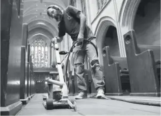  ??  ?? Parry Hardy, working for Assist2Hea­r, cuts out grout in the tile floor around the pews of St. John’s Cathedral on Wednesday. Hardy was preparing the floor to install a hearing wire that loops around a room and will connect to an in-house sound system.
