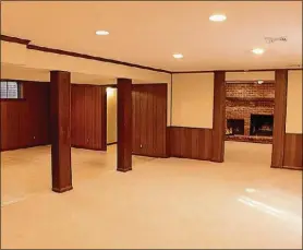  ??  ?? In the finished lower level, paneling, wood beams and flooring treatment divides the open space into a second family room and recreation room. A separate media room or sitting room has a full brick wall surroundin­g a fireplace with raised hearth and woodbeam mantel.