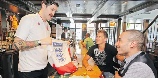  ?? JOHN MAHONEY ?? Burgundy Lion pub co-owner Paul Desbaillet­s shows an English soccer fan flag to James Hung, right, and Nick DiPatria. The pub is the official headquarte­rs for England fans.