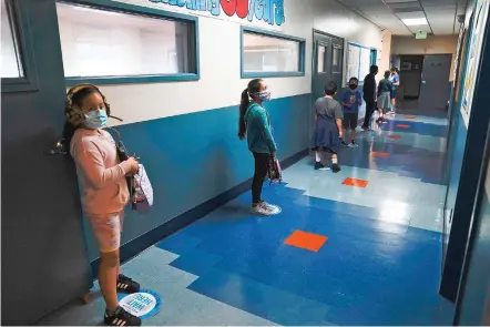  ?? ASSOCIATED PRESS FILE PHOTO ?? Los Angeles Unified School District students stand socially distanced in a hallway during a lunch break Aug. 26 at Boys & Girls Club of Hollywood in Los Angeles. California Gov. Gavin Newsom is encouragin­g schools to resume in-person education next year. He wants to start with the youngest students, and is promising $2 billion in state aid to promote coronaviru­s testing, increased ventilatio­n of classrooms and personal protective equipment.