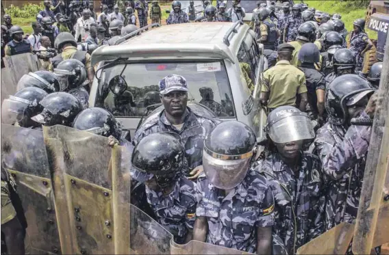  ?? Photos: Badru Katumba/afp ?? Repeat offenders: Police surround the car of Ugandan politician Bobi Wine in April 2019. Wine, a strident critic of President Yoweri Museveni (seen below on post-election posters), has been beaten and arrested numerous times for his opposition to the ruling party.