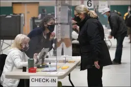  ?? STEVEN SENNE — THE ASSOCIATED PRESS FILE ?? A poll worker, center left, speaks through a plastic barrier while assisting a voter in a polling station at Marshfield High School in Marshfield, Mass., on Nov. 3, 2020.