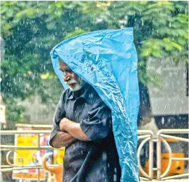  ??  ?? A man covers himself in a plastic bag as he walks in rain in the city