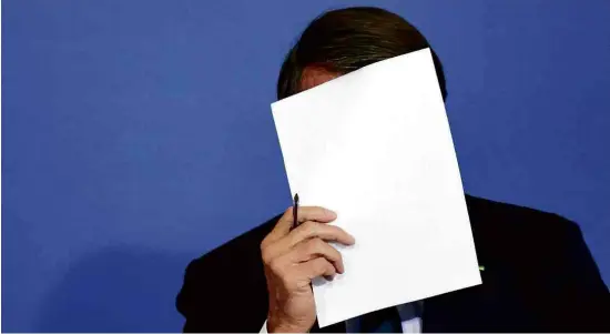  ?? Ueslei Marcelino - 20.jun.22/Reuters ?? Jair Bolsonaro com papel em frente ao rosto durante cerimônia no Palácio do Planalto, na semana passada