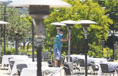  ?? Photos by Josh Edelson / Special to The Chronicle ?? Carlos Oliveria sets up heaters Wednesday for the reopening of onsite dining at Cole’s Chop House in Napa.