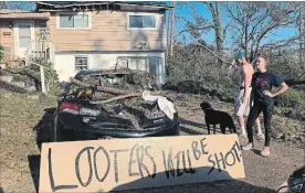  ?? BRENDAN FARRINGTON THE ASSOCIATED PRESS ?? Shauna Benefield and Alex Edwards stand near a sign warning looters in front of their house in Marianna, Fla., which was damaged by fallen trees during Hurricane Michael. Armed looters are targeting homes and businesses that remain without electricit­y.