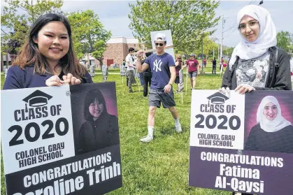  ?? DANIEL BROWN/LOCAL JOURNALISM REPORTER ?? Caroline Trinh, left, and Fatima Al-Qaysi, right, present their signs during a surprise graduation event recently at Colonel Gray High School in Charlottet­own.