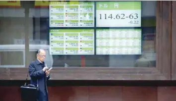  ?? — Reuters file photo ?? A man stands in front of electronic boards showing stock prices and exchange rate between Japanese Yen and US dollar outside a brokerage in Tokyo, Japan.