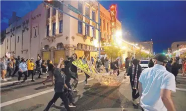  ?? ADOLPHE PIERRE-LOUIS/JOURNAL ?? Protesters march past the boarded-up windows of the KiMo Theatre in Downtown Albuquerqu­e on Tuesday evening. The venue’s windows were smashed by rioters Sunday night.