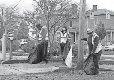  ?? BARBARA J. PERENIC/COLUMBUS DISPATCH ?? Volunteers, from left, Larry Hergins, Anthony Shanks and Ronald Griffin pick up trash behind a vacant fast food restaurant on South High Street in Columbus.