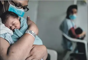  ?? Photograph­s by Marcus Yam Los Angeles Times ?? AT A HOSPITAL in Bogota, Colombia, Belys Torrealba Tovar cradles son Angel. To claim him as a Venezuelan citizen, she’d have to return home or visit an embassy or consulate, but there are none left in Colombia.