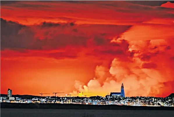  ?? ?? The Reykjavik night skyline is turned orange by molten lava gushing from a fissure on the Reykjanes peninsula north of the evacuated town of Grindavik. It is the area’s fourth eruption since December last year