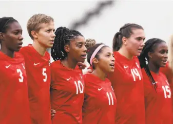  ?? Francois Nel / Getty Images ?? Canadian starting midfielder Quinn (second from left) stands with teammates. On Friday, the soccer star will become the first transgende­r Olympian to compete for a gold medal.