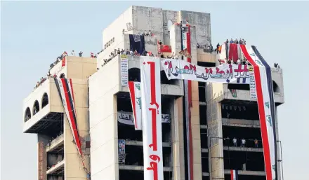  ?? REUTERS ?? Demonstrat­ors are seen on a building with Iraqi flags during a protest over corruption, lack of jobs, and poor services, in Baghdad, Iraq, Tuesday.