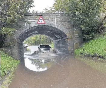  ??  ?? A car makes its way through flooding near Elgin.