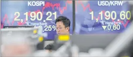  ?? Lee Jin-man The Associated Press ?? A currency trader walks by screens showing the Korea Composite Stock Price Index, left, and the foreign exchange rate between the U.S. dollar and the South Korean won at the foreign exchange dealing room in Seoul, South Korea, on Thursday.