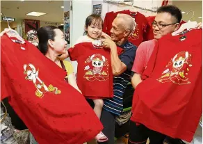  ??  ?? Red is in again: (From left) chok with her daughter, father-in-law and Paul looking at the rat themed T-shirts during at sunshine square in bayan baru, Penang.