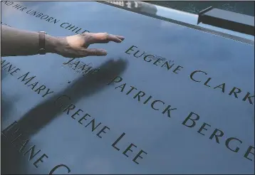  ?? (AP/Mark Lennihan) ?? Desiree Bouchat reaches towards the inscribed name of James Patrick Berger at the National September 11 Memorial, in New York. She last saw her co-worker on the 101st floor of the trade center’s south tower. Nearly 180 Aon Corp. workers died Sept. 11, 2001, including Berger. “Some days, it feels like it happened yesterday,” Bouchat says.