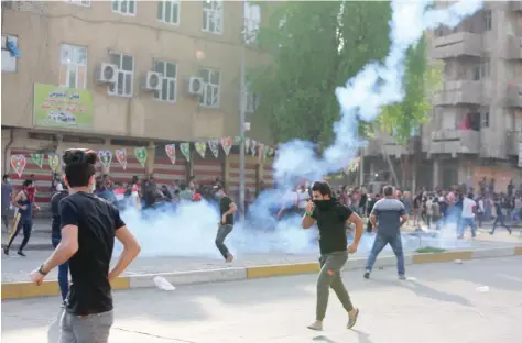  ?? — AFP ?? Iraqi protesters cover their faces from tear-gas canisters fired by Iraqi police during a demonstrat­ion at Tayaran square in Baghdad.