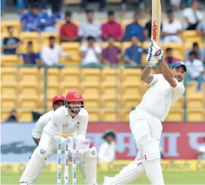  ?? AFP ?? Shikhar Dhawan hits a boundary as Afghanista­n wicketkeep­er Afsar Khan looks on during the one-off Test in Bangalore. —