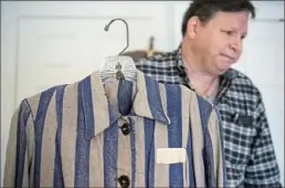  ?? Steph Chambers/Post-Gazette ?? Howard Cohen, a retired Jewish optometris­t, holds up a woman’s concentrat­ion camp uniform from his private collection of artifacts.