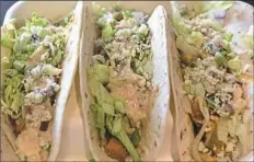  ??  ?? Buffalo chicken tacos are topped with spicy blue cheese sauce, shredded lettuce, shaved celery, red onion and crumbled blue cheese.