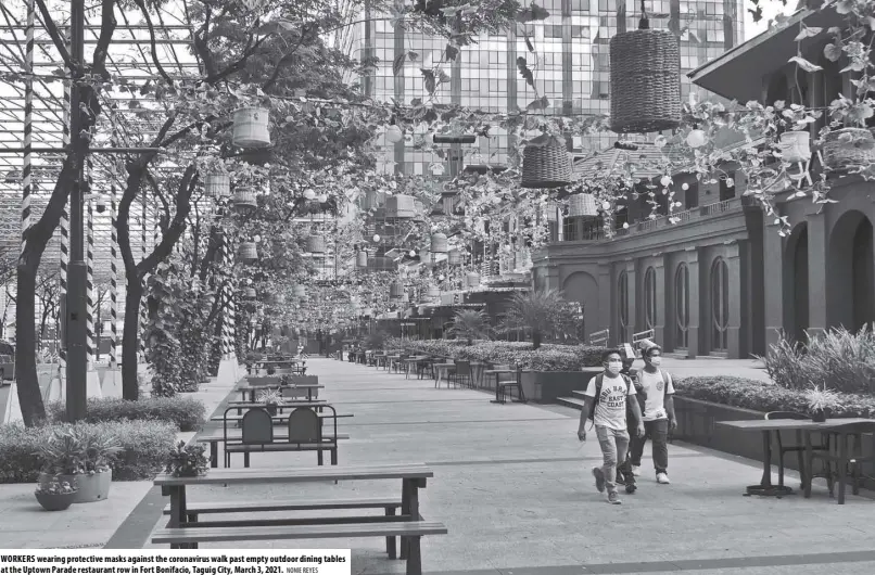  ?? NONIE REYES ?? WORKERS wearing protective masks against the coronaviru­s walk past empty outdoor dining tables at the Uptown Parade restaurant row in Fort Bonifacio, Taguig City, March 3, 2021.