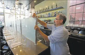  ?? Rick Bowmer / Associated Press ?? Mark Sylvester takes down a partition known as a Zion Curtain that prevent customers from seeing their drinks being mixed and poured at Current Fish & Oyster in Salt Lake City.