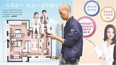  ?? AFPPIC ?? A man checking his phone outside a bank advertisin­g mortgages in Hong Kong yesterday. –