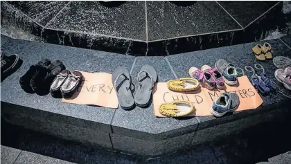  ?? ASHLEY FRASER • POSTMEDIA NEWS ?? ABOVE: People came and went from Parliament Hill in Ottawa on Sunday, leaving behind shoes they set along the Centennial Flame in honour of the 215 children whose remains were found at the property of a residentia­l school in Kamloops, B.C.
RIGHT: Eva Lucassie held Inuuya Lucassie, who will soon be three years old, as they watched people place shoes. The federal government and communitie­s all across Canada have lowered flags to half-mast in honour of the children.