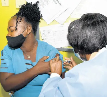  ?? KENYON HEMANS/PHOTOGRAPH­ER ?? Community health aide Kadian Esson-Valentine from the Windward Road Health Centre looks away as she prepares to receive her first COVID-19 shot from public health nurse Lorraine Holt at the Kingstonba­sed health centre yesterday.