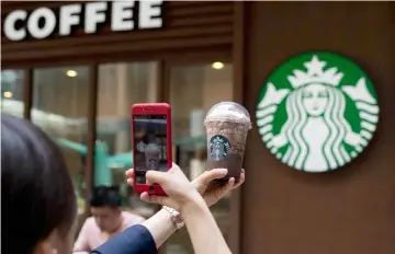  ??  ?? A woman takes a picture of her beverage at a Starbucks coffee shop in Beijing. — AFP photo