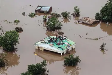  ??  ?? Desperate: People scramble on to the roof of a building in flooded Beira, Mozambique