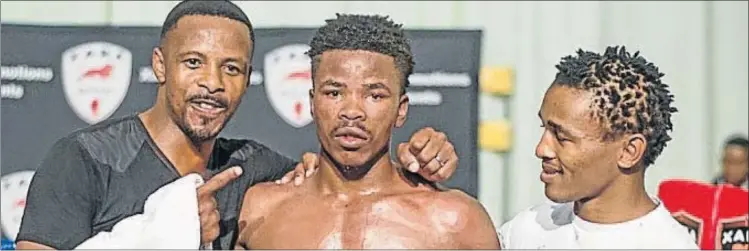  ??  ?? CENTRE OF ATTRACTION: Xolisani Mcotheli is flanked by his trainers after his sensationa­l stoppage win over Khumbulani Mdletshe at Orient Theatre in April