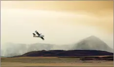  ?? LETHBRIDGE HERALD PHOTO IAN MARTENS ?? An Alberta Wildfire airtanker flies off with a load of water from the Waterton Reservoir as smoke rises from the mountainsi­de and grasslands in Waterton Lakes National Park.