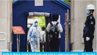  ?? — AFP (See Page 8) ?? BEIJING: An official in a hazmat suit waits inside a high school as a student arrives yesterday.