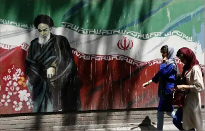  ?? Atta Kenare/AFP/Getty Images ?? Iranians walk by a mural painting of the founder of the Islamic Republic, Ayatollah Ruhollah Khomeini, on the wall of the former U.S. embassy in Tehran.