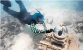  ?? WILFREDO LEE/AP ?? Marine biologist Colin Foord uses a toothbrush to clean the glass on the Coral City Camera along a rock wall in Miami. Foord and J.D. McKay have been on a 15-year mission to raise awareness about dying coral reefs with a company that presents the issue through science and art, including livestream­s of coral set to music, video images projected on buildings and a psychedeli­c line of coral-themed clothing.