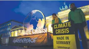  ??  ?? Greenpeace activists stand near to a giant globe installati­on erected in front of Berlin’s Brandenbur­g Gate yesterday.