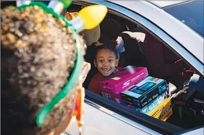  ?? PHOTOS BY WADE VANDERVORT ?? A child receives toys and shoes from a volunteer during a drive-thru charity event Thursday at Martinez Elementary School in North Las Vegas. The drive was sponsored by local philanthro­pists Bob and Sandy Ellis.