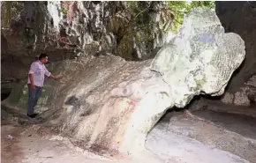  ??  ?? Turned to stone: Ahmad touching the stone formation resembling a reclining buffalo at Kampung Kodiang Lama near Jitra, Kedah. — Bernama