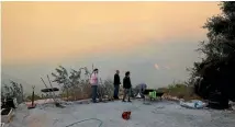  ?? REUTERS ?? Residents are seen at the courtyard outside their house in Nataf as wildfire burns on the hills and mountains around it, outside Jerusalem.