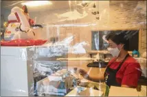  ??  ?? Owner Jane Chung stands behind two clear protective curtains as she rings up a customer at her store inside the Atlanta Chinatown Shopping Mall in Chamblee. In the pandemic, Chung relies on takeout orders and struggles to pay her workers.